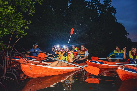  group of kayakers enjoy the twilight hues reflecting on the water's surface as they navigate through Bali's mangroves at dusk.