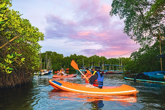 Kayakers wearing life jackets group together on the water, illuminated by the soft glow of their headlamps under the darkening Bali sky.