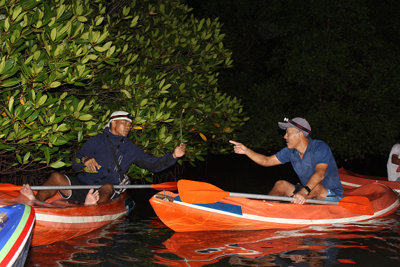 Two kayakers engaging with each other during a night tour in Bali's mangrove forest, sharing a moment of camaraderie.