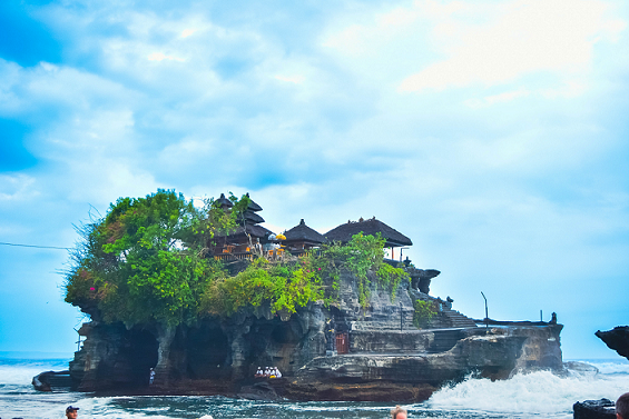 Close-up of the same Balinese temple on a rocky outcrop, with waves crashing around it, showcasing detailed temple architecture and lush greenery.