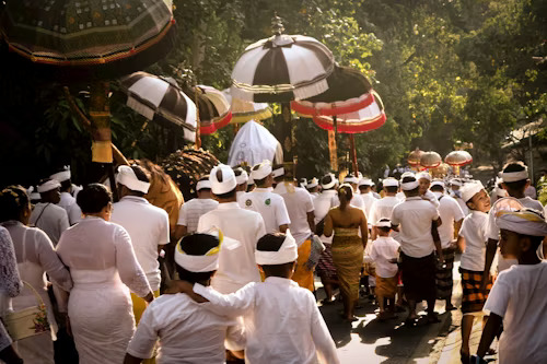 A ceremonial procession in Bali with participants dressed in traditional Balinese attire, including white garments, sarongs, and headpieces, as they walk through a vibrant and sacred ritual event, showcasing the island’s rich spiritual heritage.