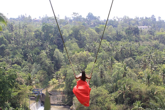 Woman in a flowing red dress on the Bali Swing, soaring above lush jungle scenery for a breathtaking view in Bali