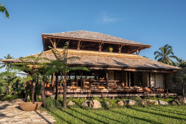 Exterior view of Begawan Biji Restaurant in Bali, showcasing the traditional wooden architecture, surrounded by lush greenery and palm trees