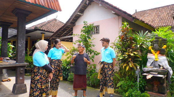 Visitors engaging in a cultural exchange with a local Balinese elder in a traditional village setting, surrounded by lush greenery and authentic Balinese architecture.