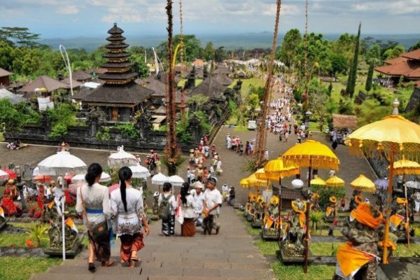 Visitors in traditional Balinese attire walk down the grand staircase of Besakih Temple, Bali’s largest and holiest temple complex, adorned with colorful ceremonial umbrellas and offerings during a vibrant temple festival