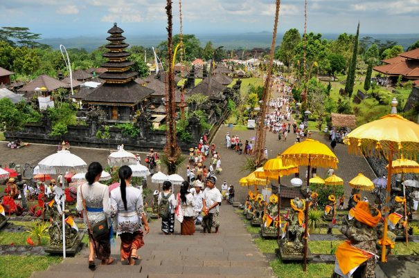 Visitors in traditional Balinese attire walk down the grand staircase of Besakih Temple, Bali’s largest and holiest temple complex, adorned with colorful ceremonial umbrellas and offerings during a vibrant temple festival