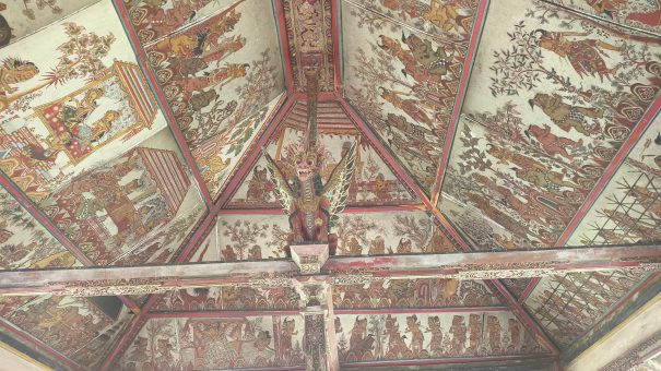 Intricate ceiling paintings of Kertha Gosa Pavilion in Bali, featuring traditional Kamasan-style art depicting scenes of justice and morality, with a central Garuda figure — a highlight of any Bali heritage tour
