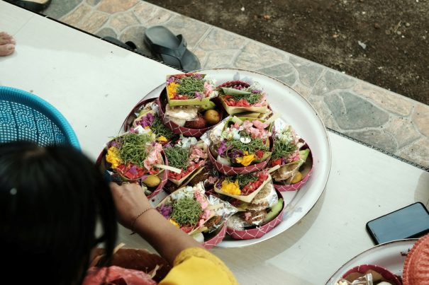 (English) Balinese Offering Workshop in Ubud: A Meaningful Cultural Experience Balinese woman preparing Canang Sari offerings with colorful flowers and natural elements during a traditional offering class in Ubud