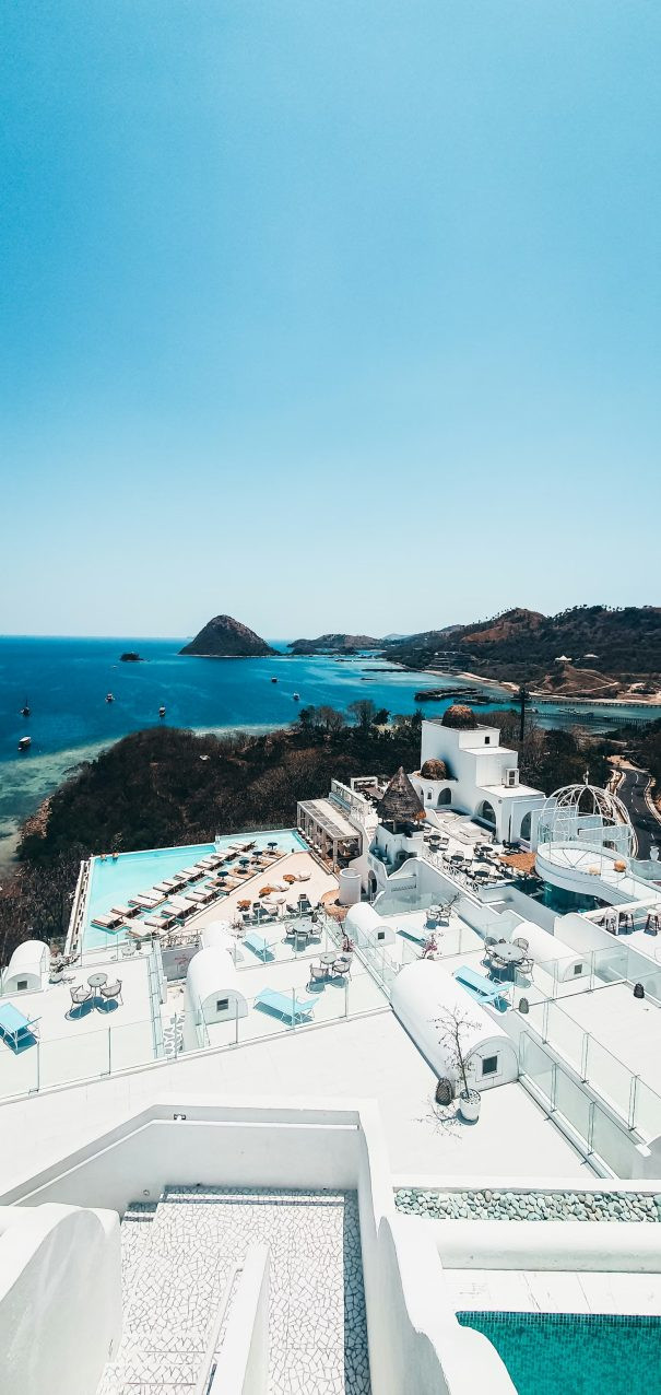 From above, a seafront hotel in Labuan Bajo showcases bright white terraces set against the blue sea and rugged island landscape.