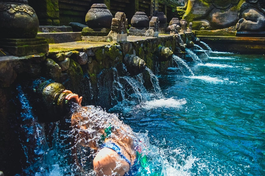 A person participating in the purification ritual at Tirta Empul Temple, where water flows from the sacred spouts into the pool, symbolizing spiritual cleansing in Balinese Hindu tradition.