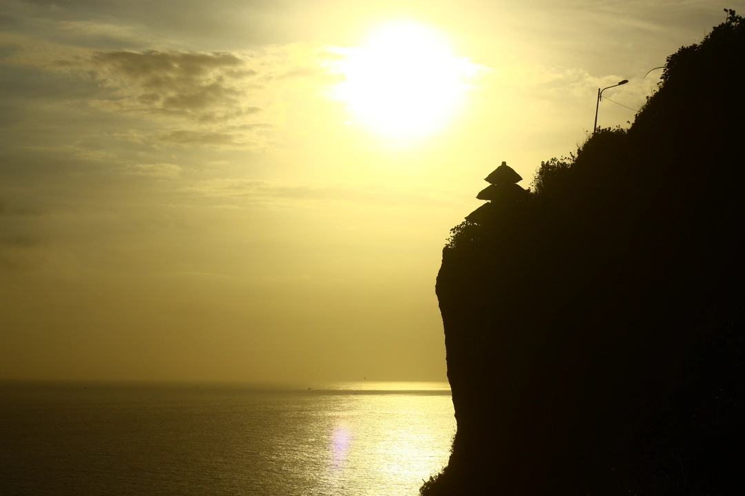 Silhouette of Uluwatu Temple at sunset, perched on a cliff overlooking the serene Indian Ocean