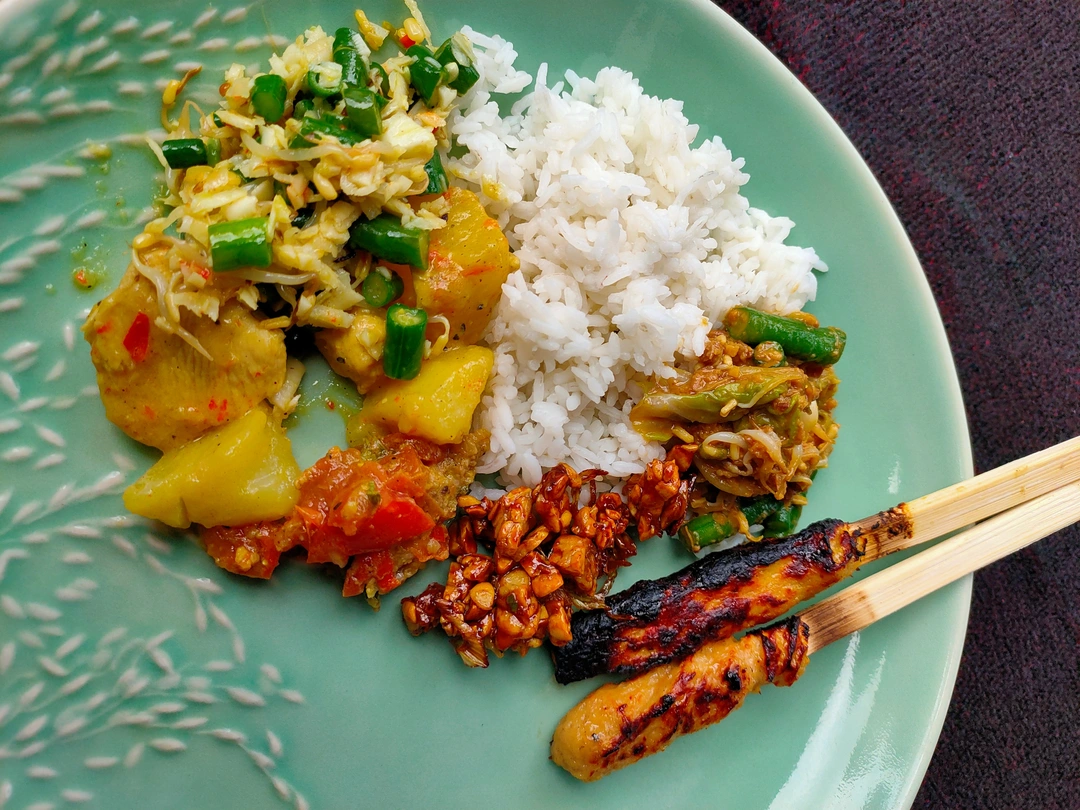 A plate of Indonesian cuisine featuring white rice, mixed vegetable curry, spicy minced meat, and a grilled satay skewer with char marks, presented on a turquoise ceramic plate, ready to be enjoyed