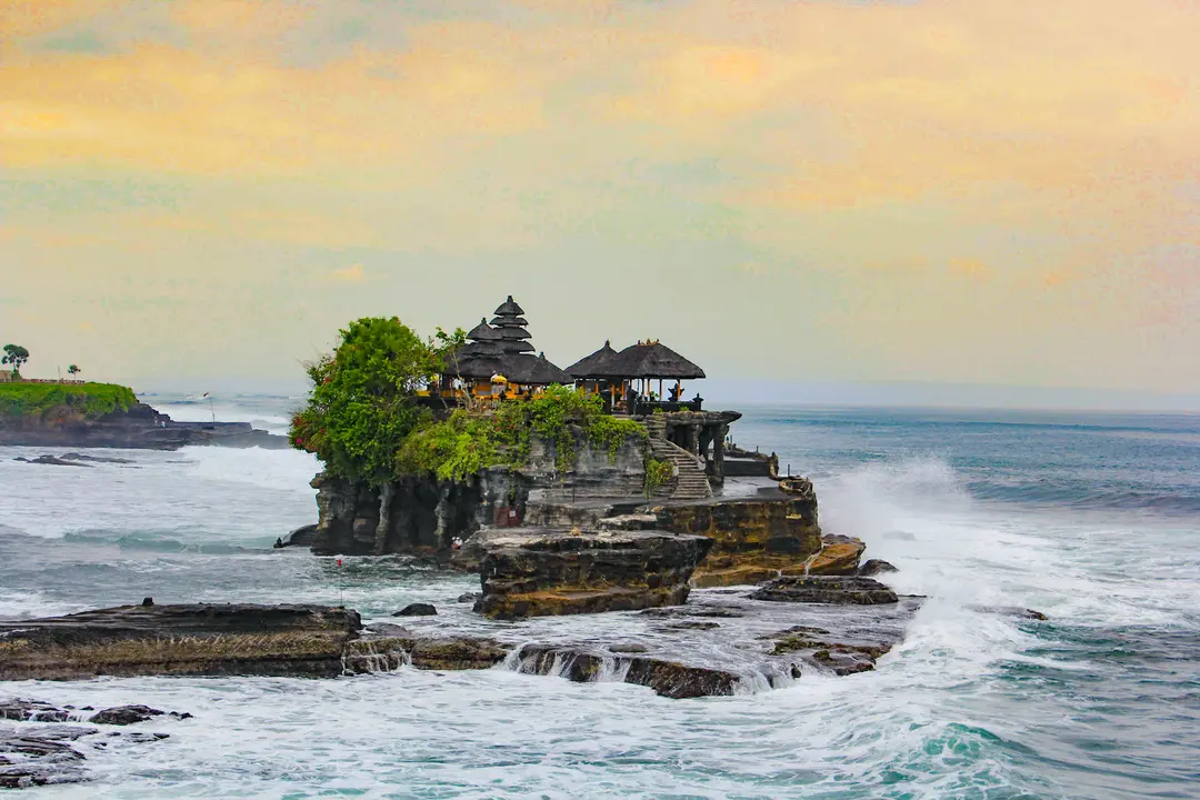 Iconic Tanah Lot Temple, a serene and mystical spot, perched on a rocky outcrop, bathed in the golden glow of the setting sun - Charter Car - Kura-Kura Bus